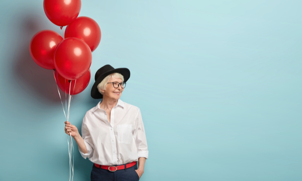 A woman is smiling and holding a bouquet of red balloons. She is ready to celebrate her retirement.