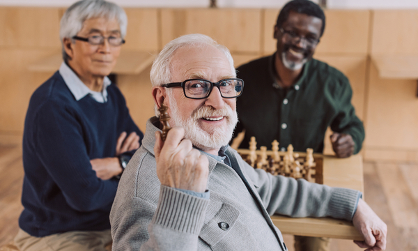 RTOERO Foundation supports social engagement of senior through community grants and funding. A group of older gentlemen smiling and engaged in a game of chess. 