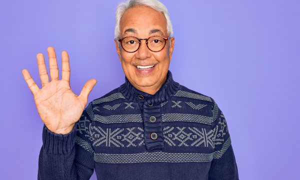 A smiling middle-aged man is wearing glasses and holding up five fingers.