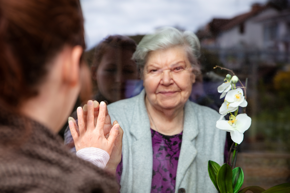 A younger family member is having a window visit with a older member during the pandemic.