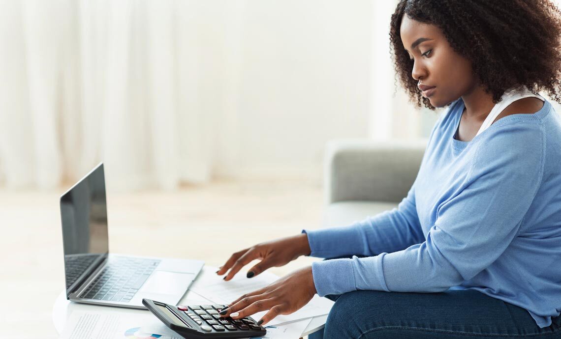 A woman working on her retirement plan. She’s using a calculator and has a laptop open in front of her