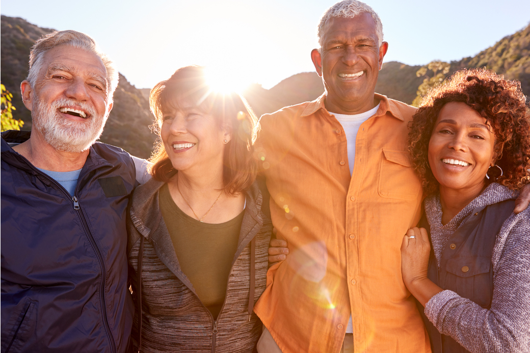 Quatre amis retraités souriant et se promenant ensemble dans la campagne.