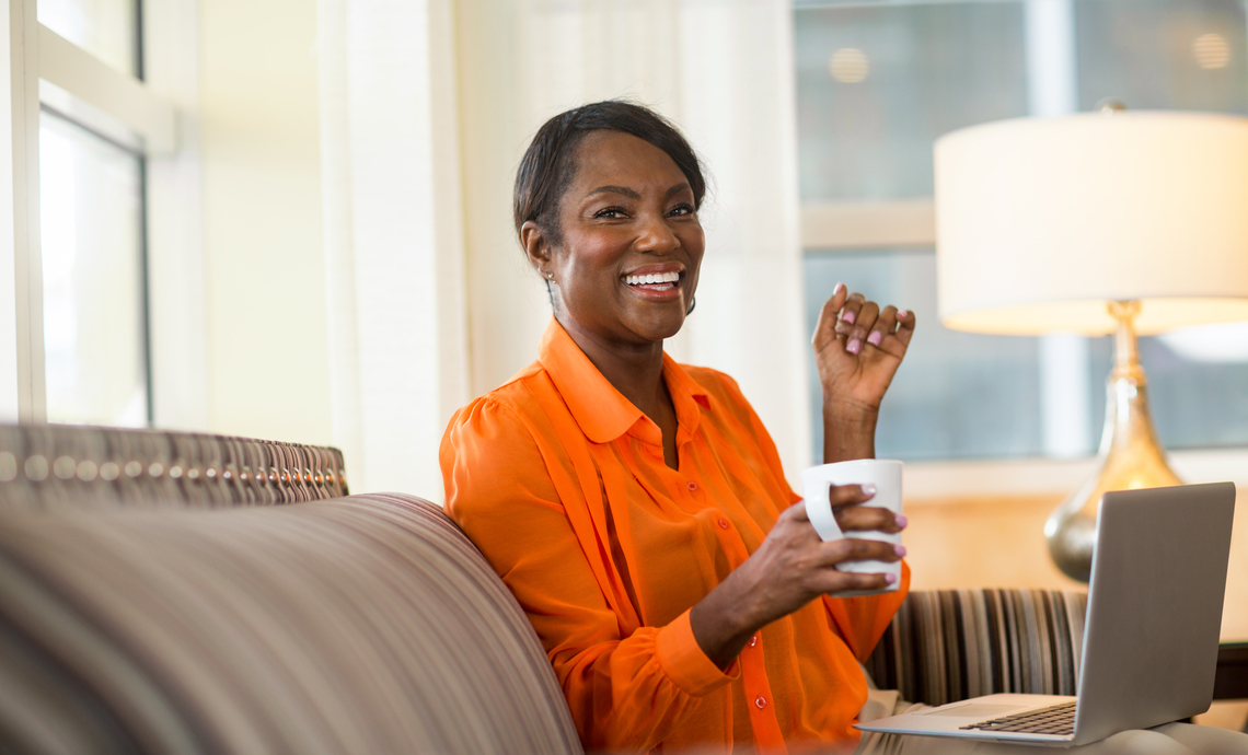 Education sector worker sitting on a couch and researching retirement planning info on laptop