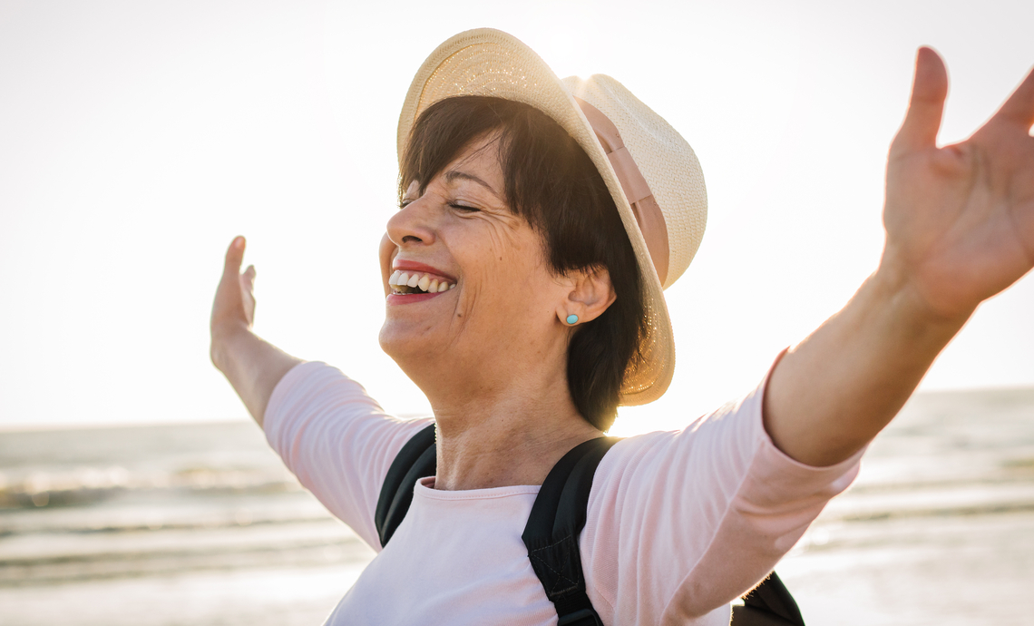 A recent retiree enjoying the freedom of the beach standing with open arms and a happy smile.