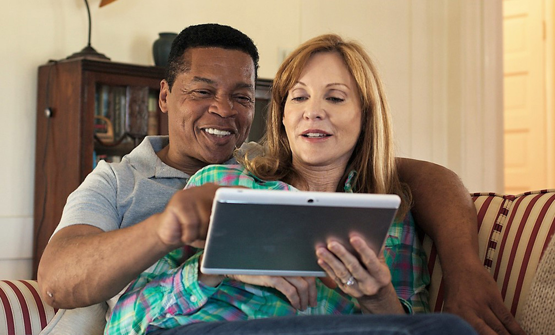 A biracial older couple cuddling together on a couch and using a tablet to research tax credits available to them.