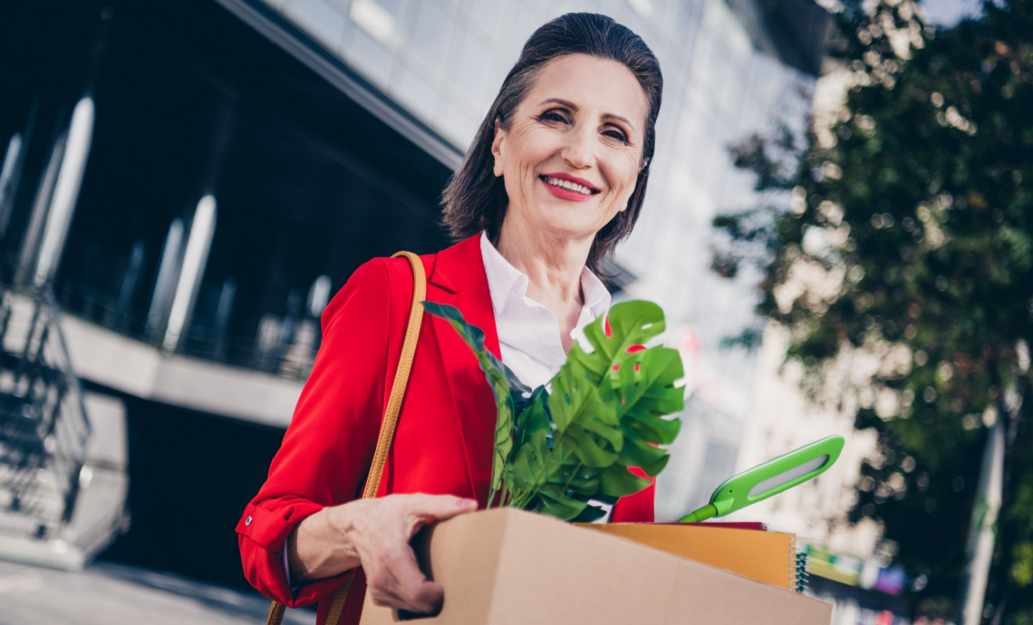 Personne à la retraite qui porte le contenu de son bureau dans une boîte et qui quitte son travail avec le sourire