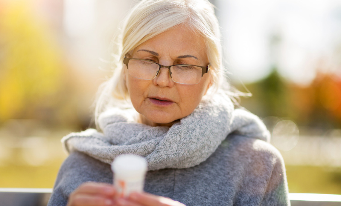 Older adult sitting outside and looking at the label on a prescription bottle
