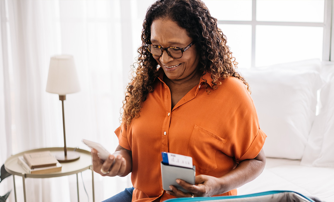 Education retiree sitting on bed in bedroom and looking at ticket for first trip in retirement