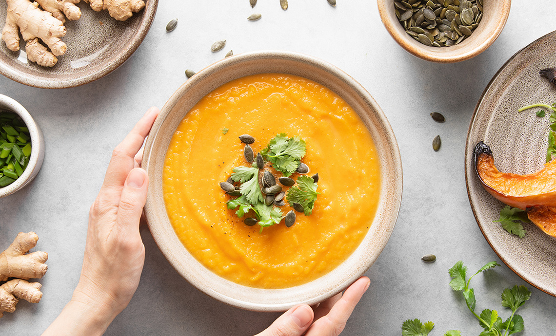 Hands holding a bowl of pumpkin soup